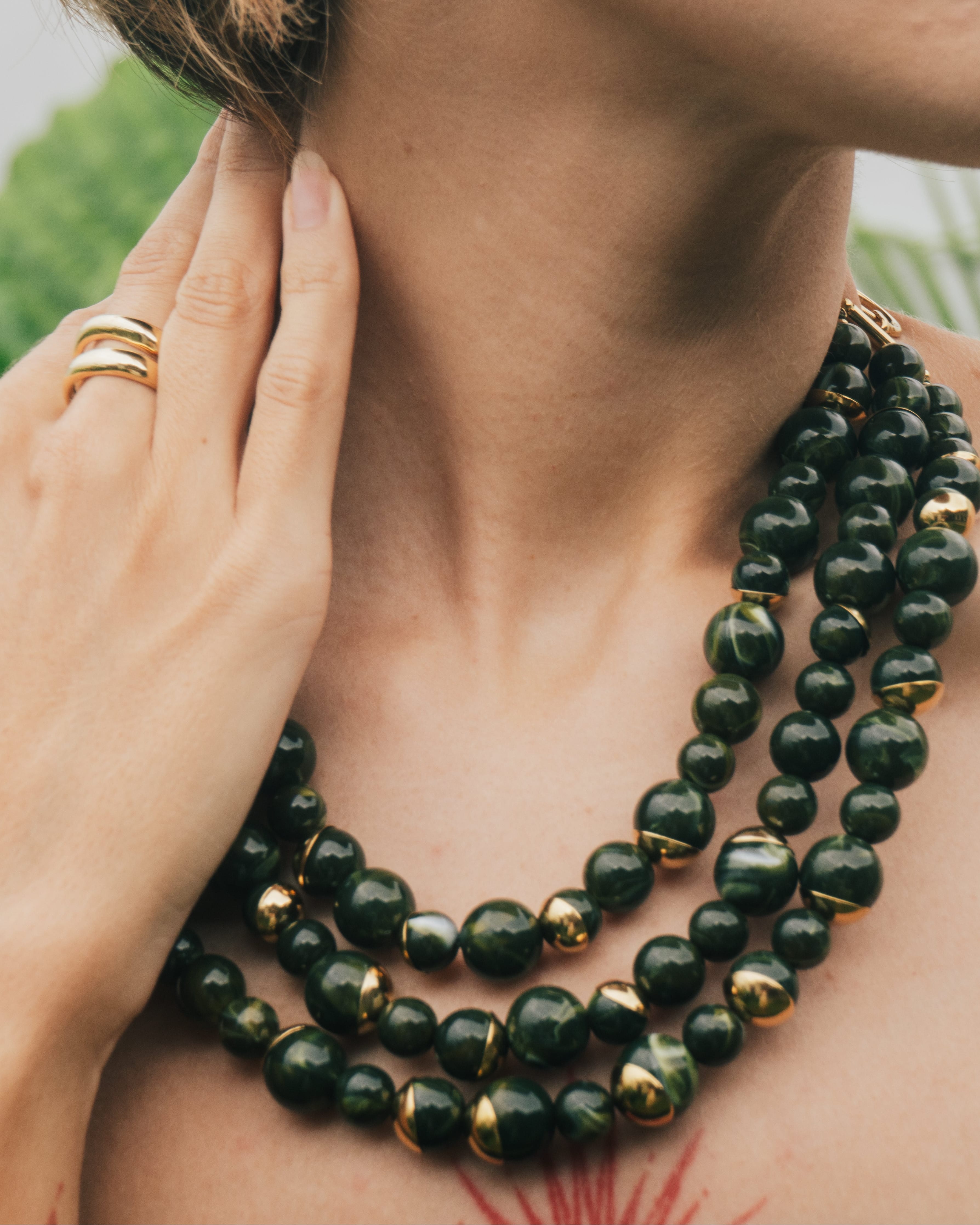 Close-up of a person wearing a green beaded necklace with gold accents.