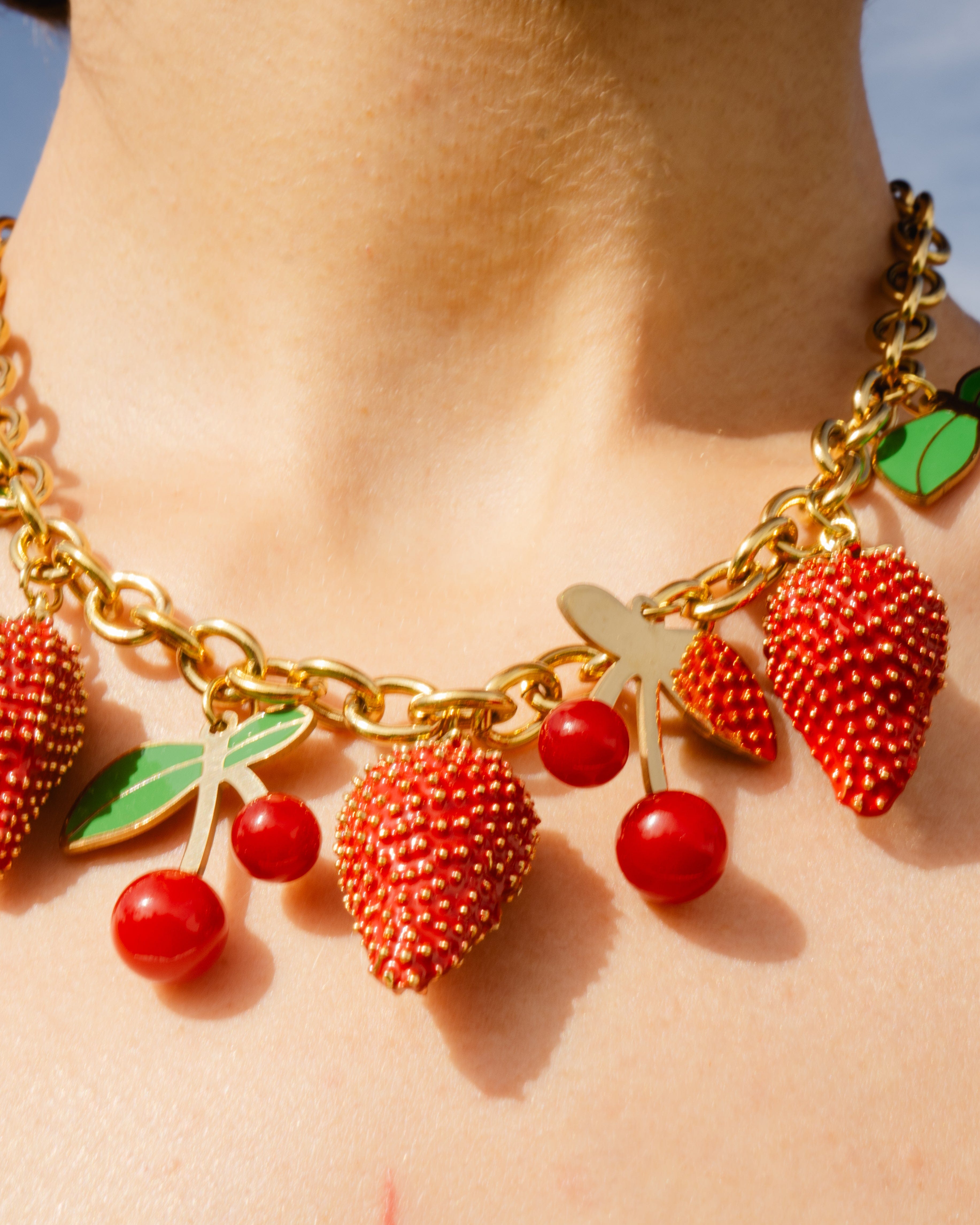 Gold necklace with strawberry, cherry, and leaf charms on a person's neck.