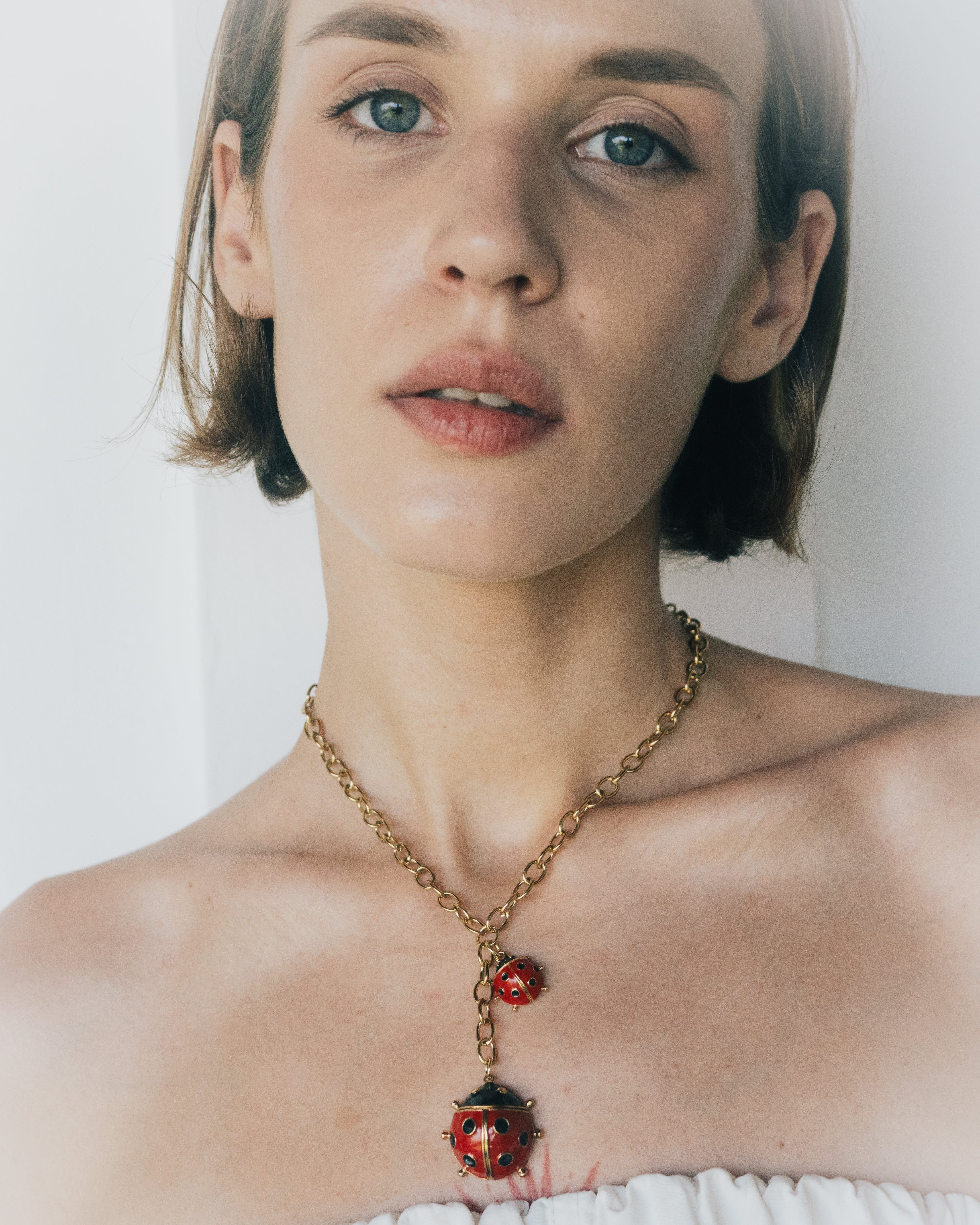 Woman wearing a necklace with ladybug pendants against a white background