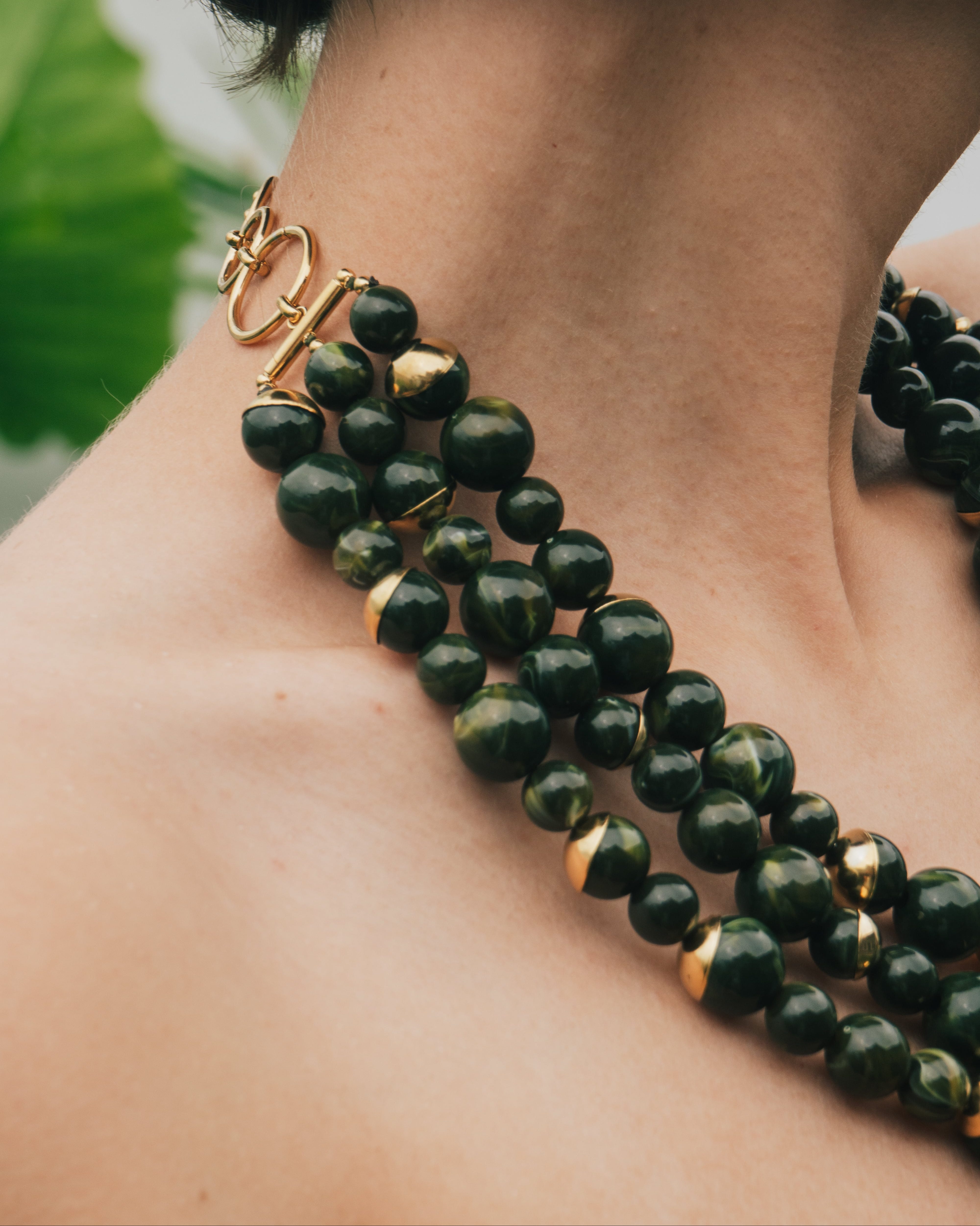 Close-up of a green beaded necklace with gold accents on a person's neck.
