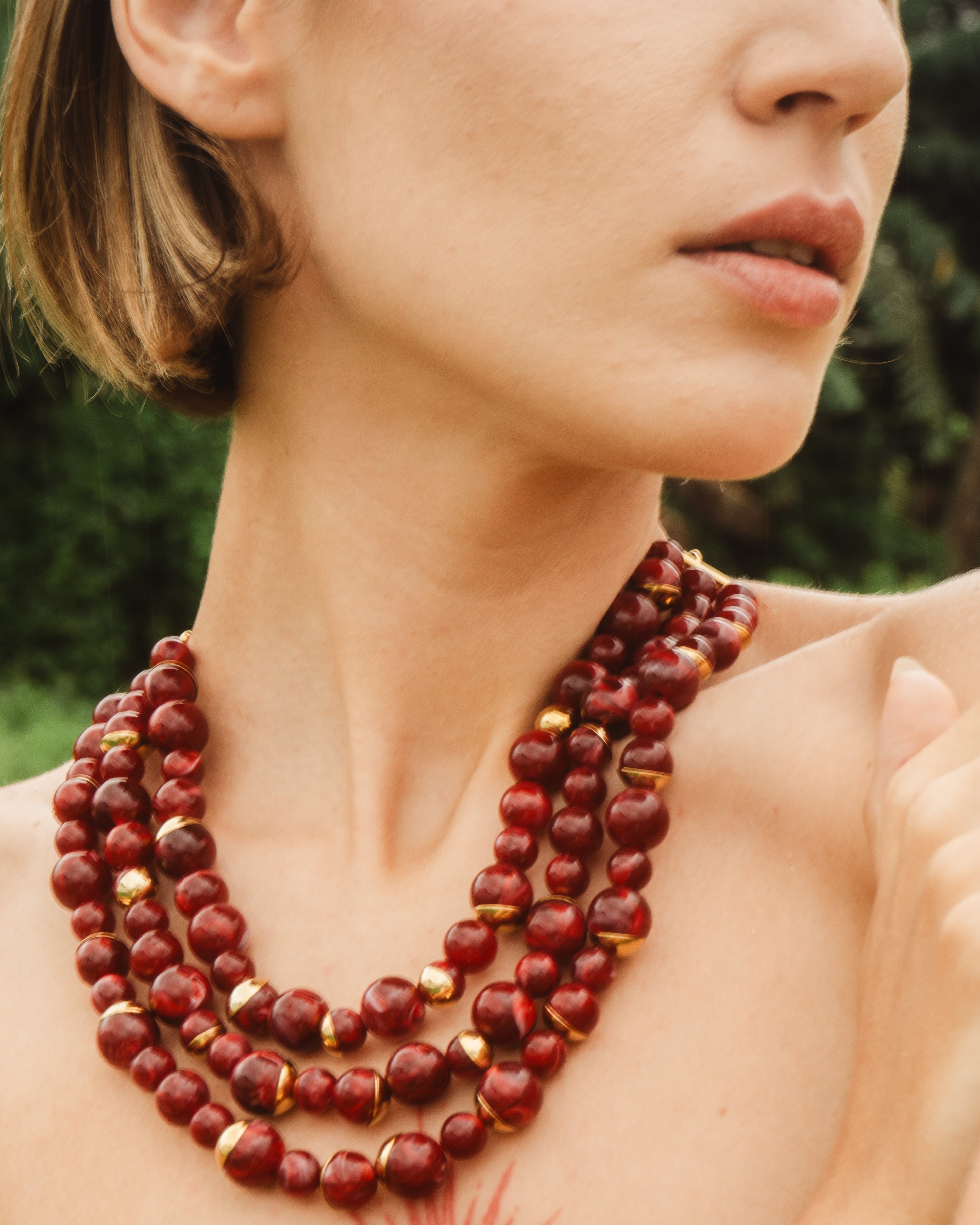 Woman wearing a red beaded necklace with a blurred green background