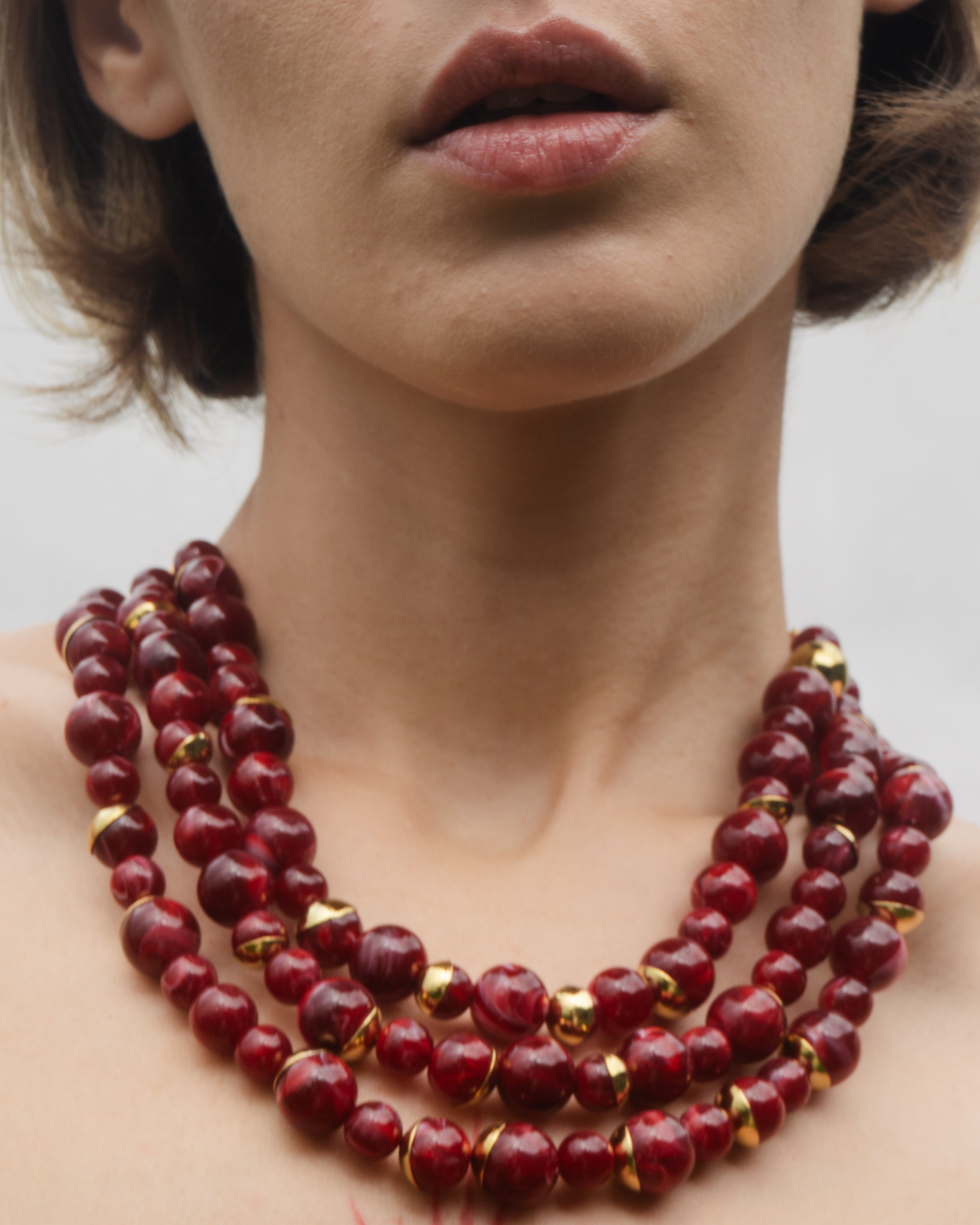 Close-up of a woman wearing a red beaded necklace with gold accents.