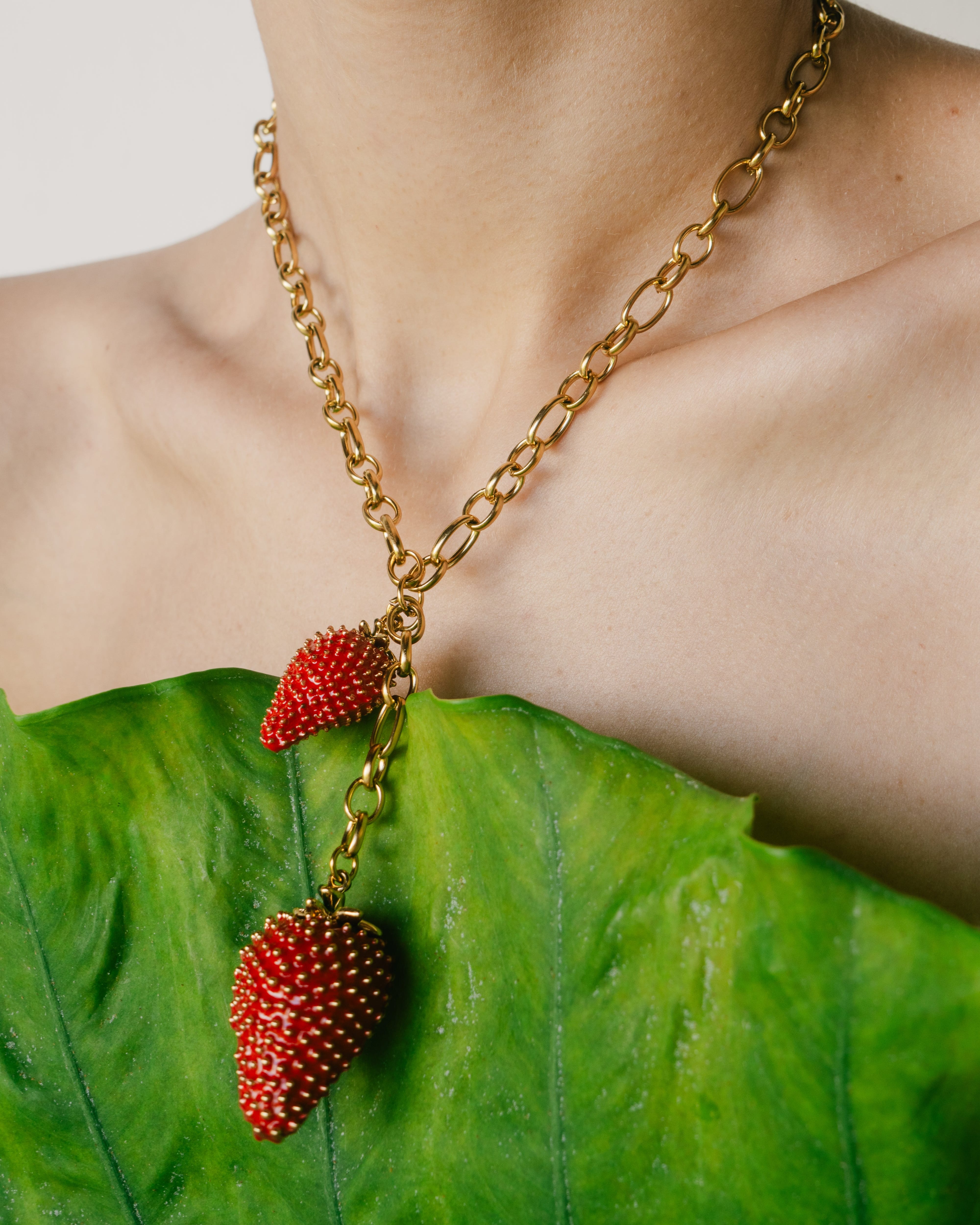 Necklace with strawberry pendants on a person against a green leaf background