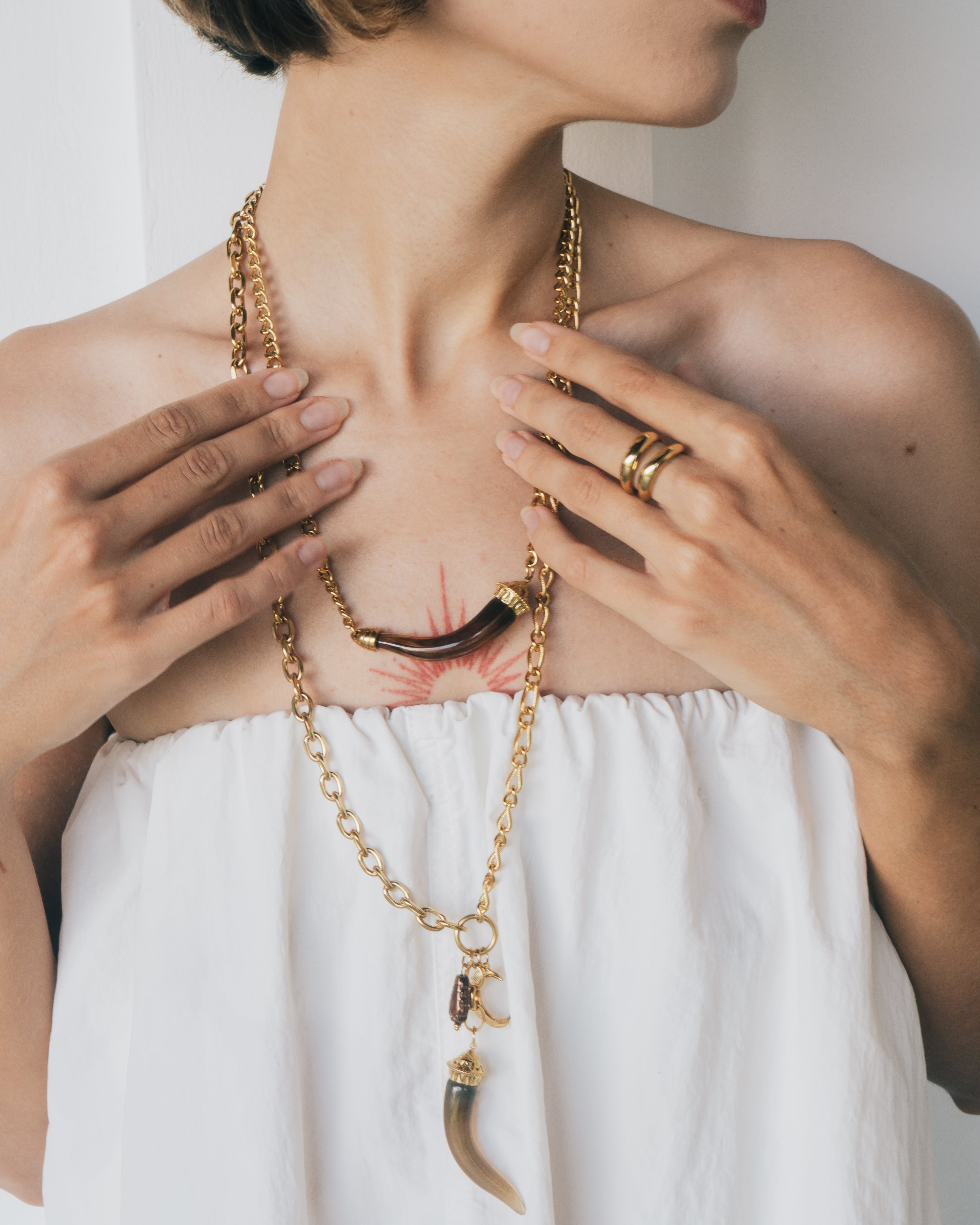 Person wearing a gold necklace with a white garment, focusing on jewelry.