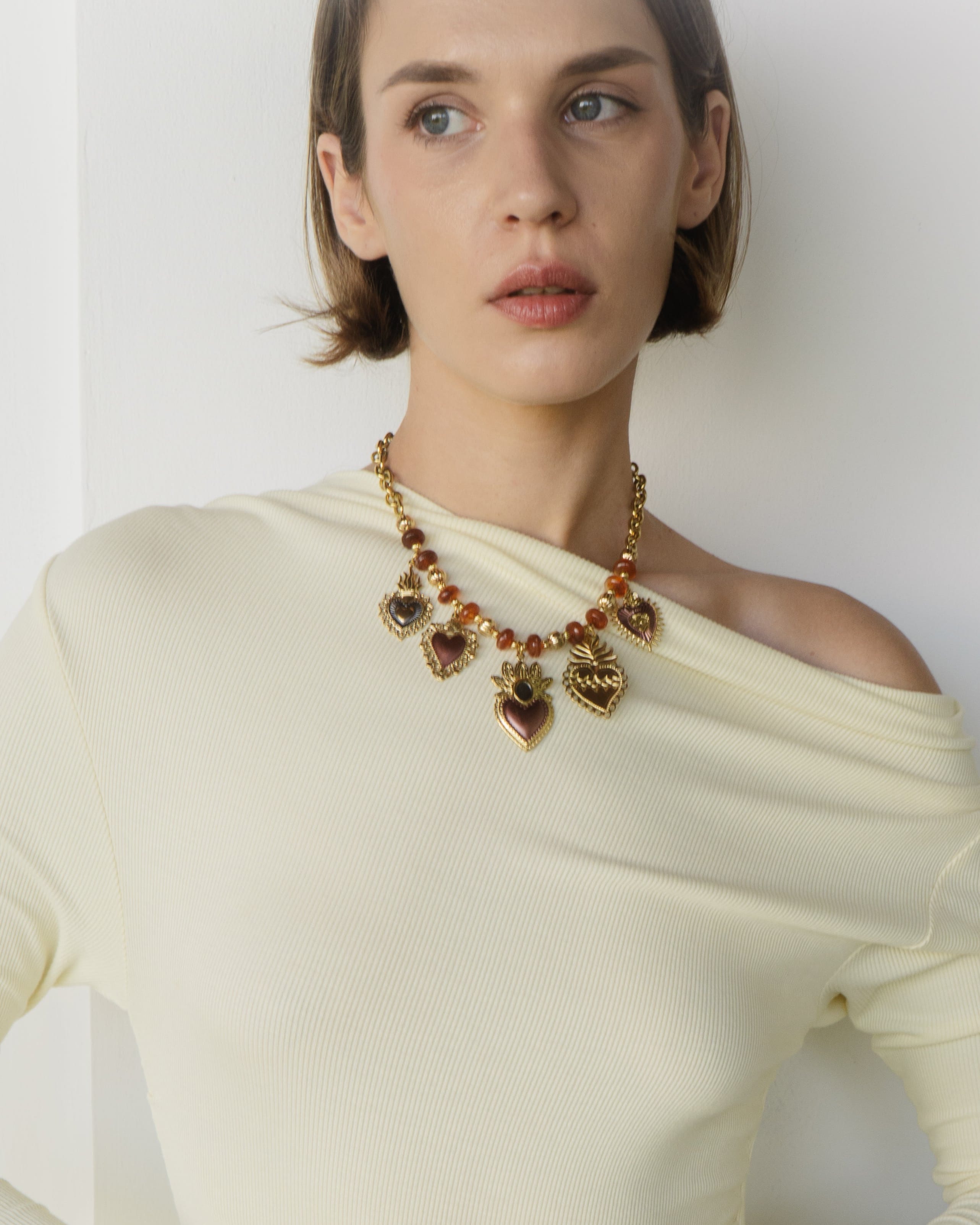 Woman wearing a cream-colored dress with long sleeves and a necklace against a white background