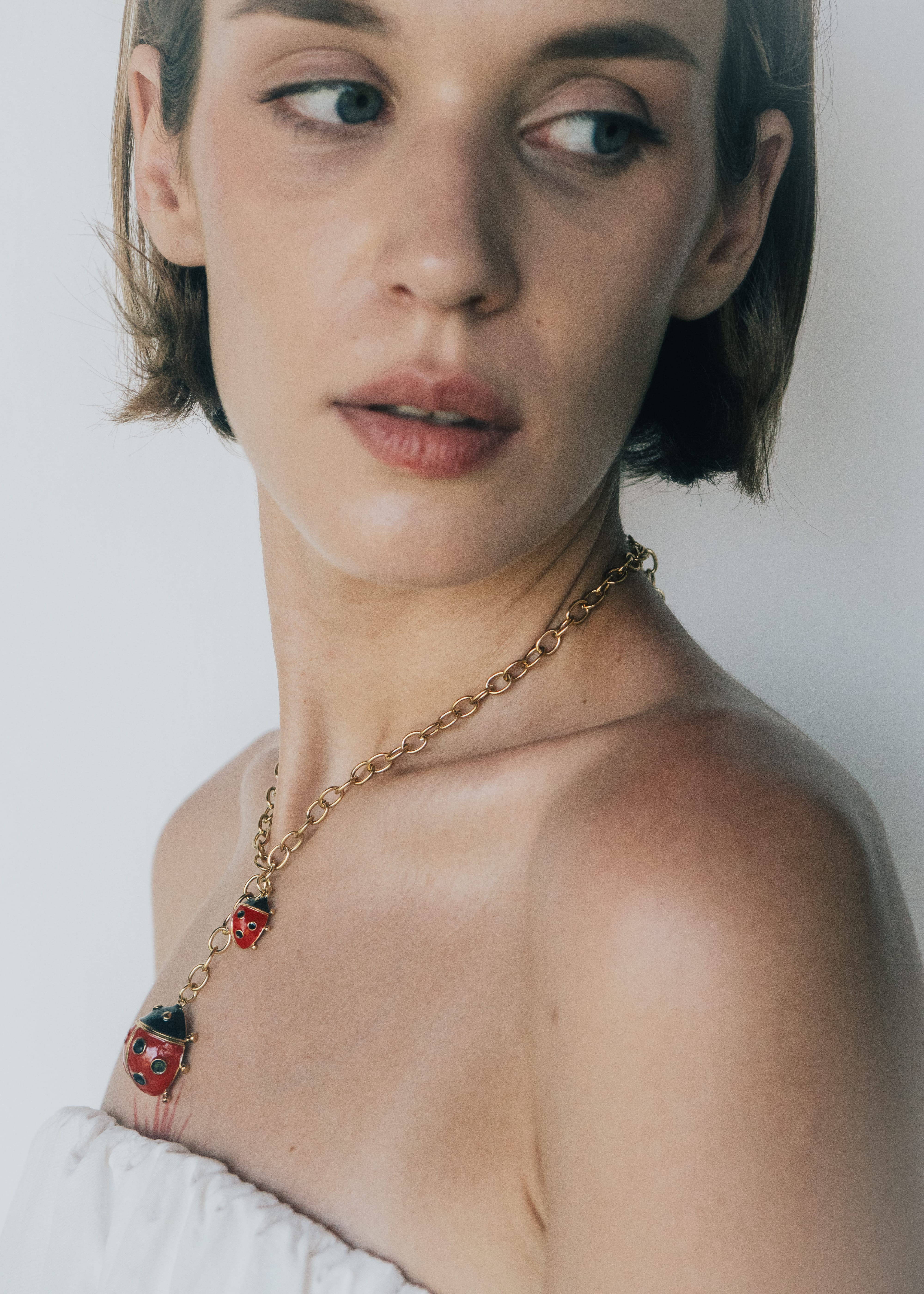 Woman wearing a gold necklace with ladybug pendants against a plain background