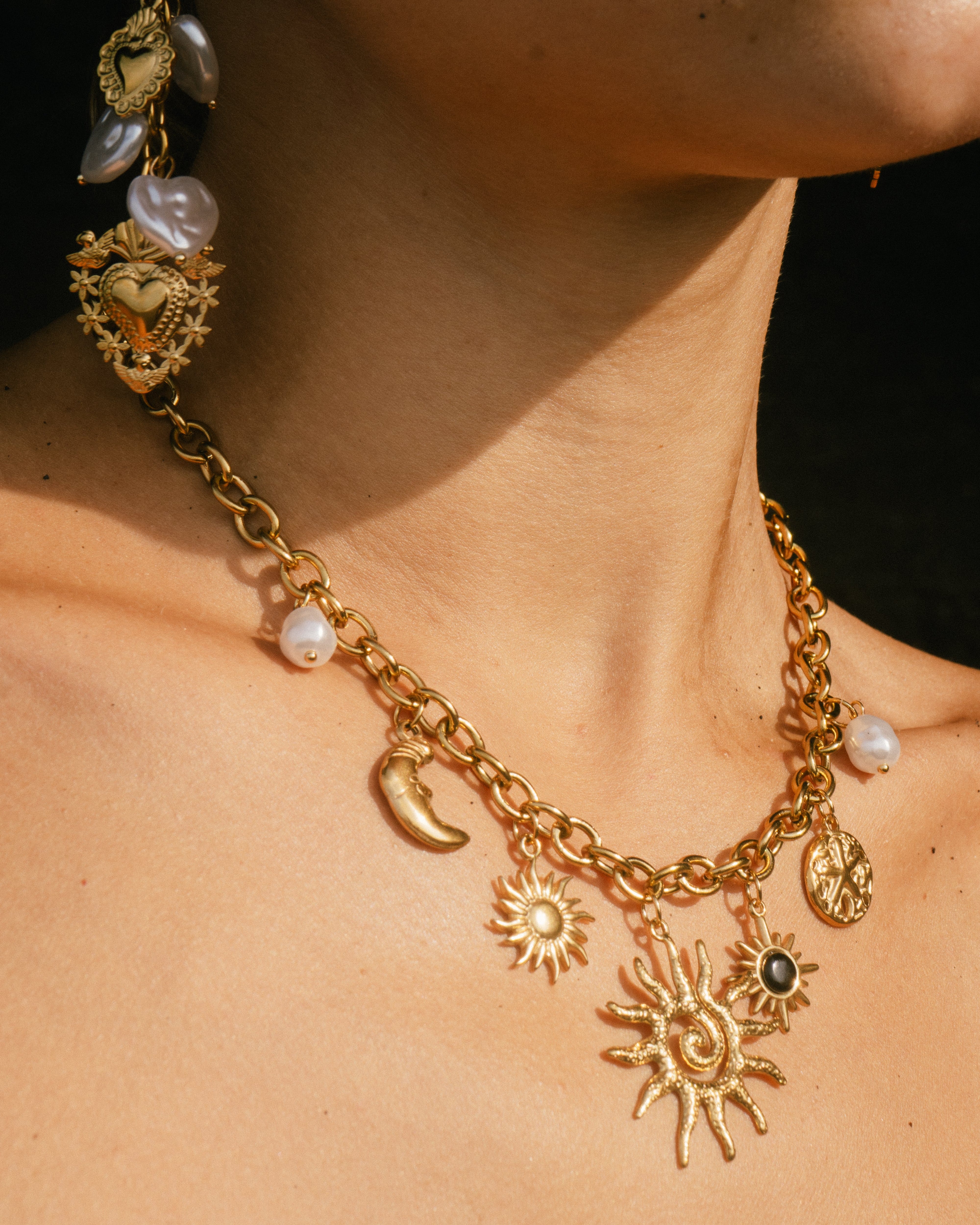 Gold necklace with various charms on a person's neck against a black background